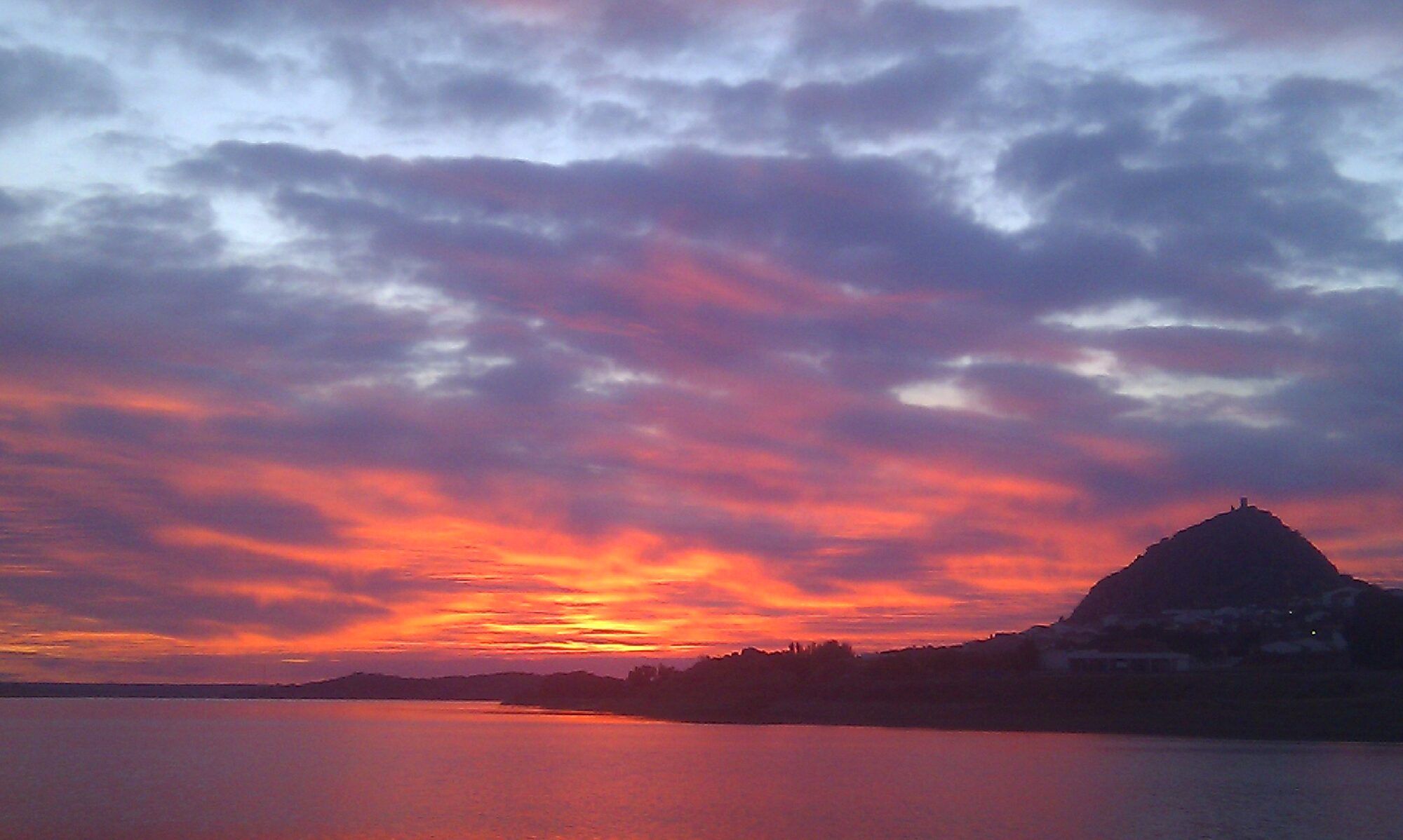 El cerro del castillo recortado sobre el embalse en un atardecer rojo