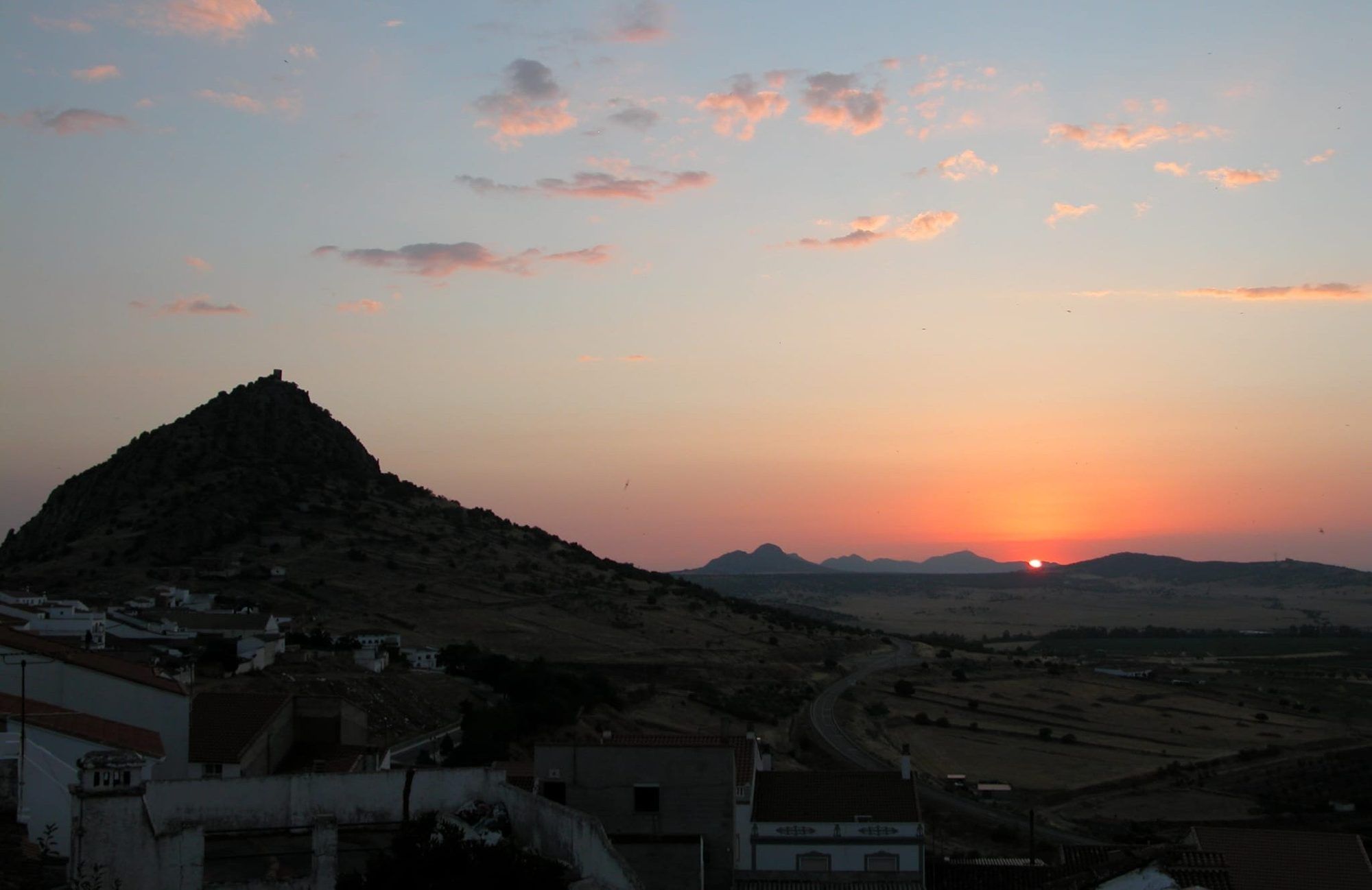 El sol poniéndose junto al cerro del castillo, visto desde los tejados del pueblo