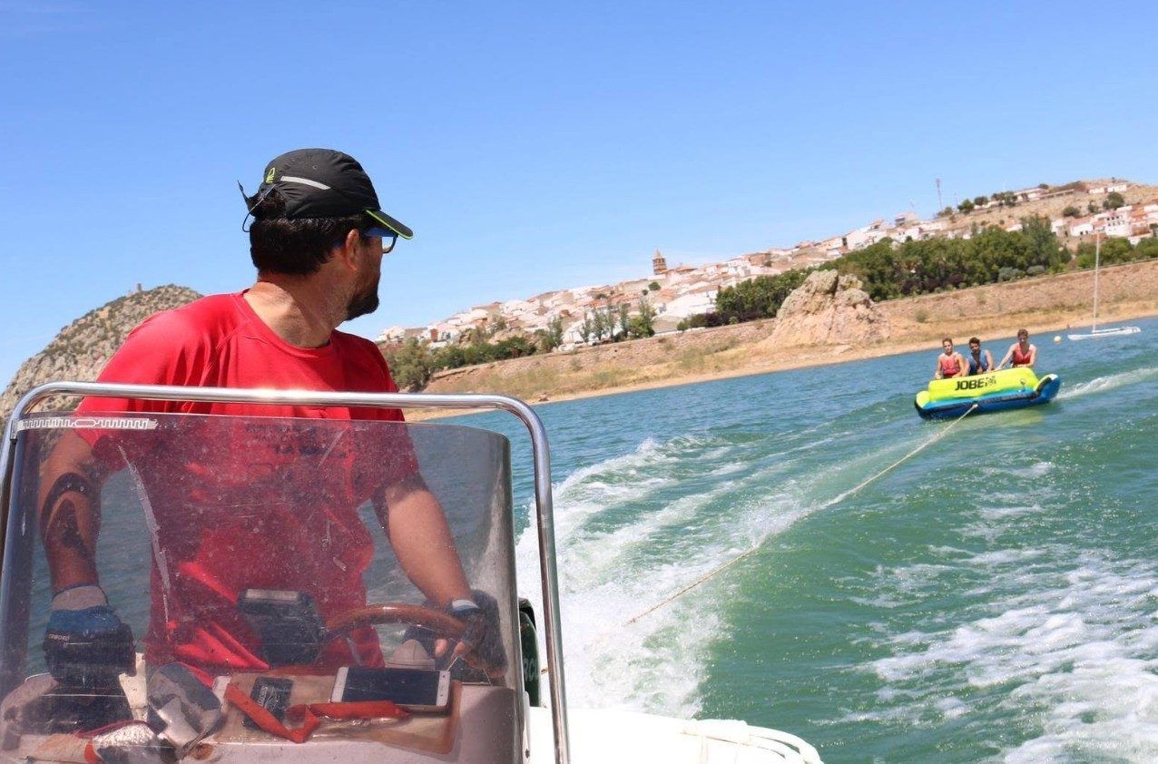 Banana hinchable remolcada por una lancha en el embalse, con el pueblo al fondo