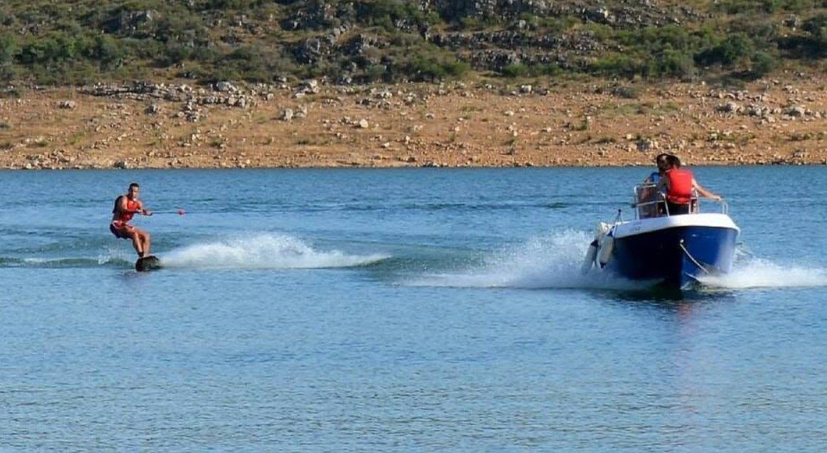 Una persona sobre la tabla, remolcada por una lancha en el embalse