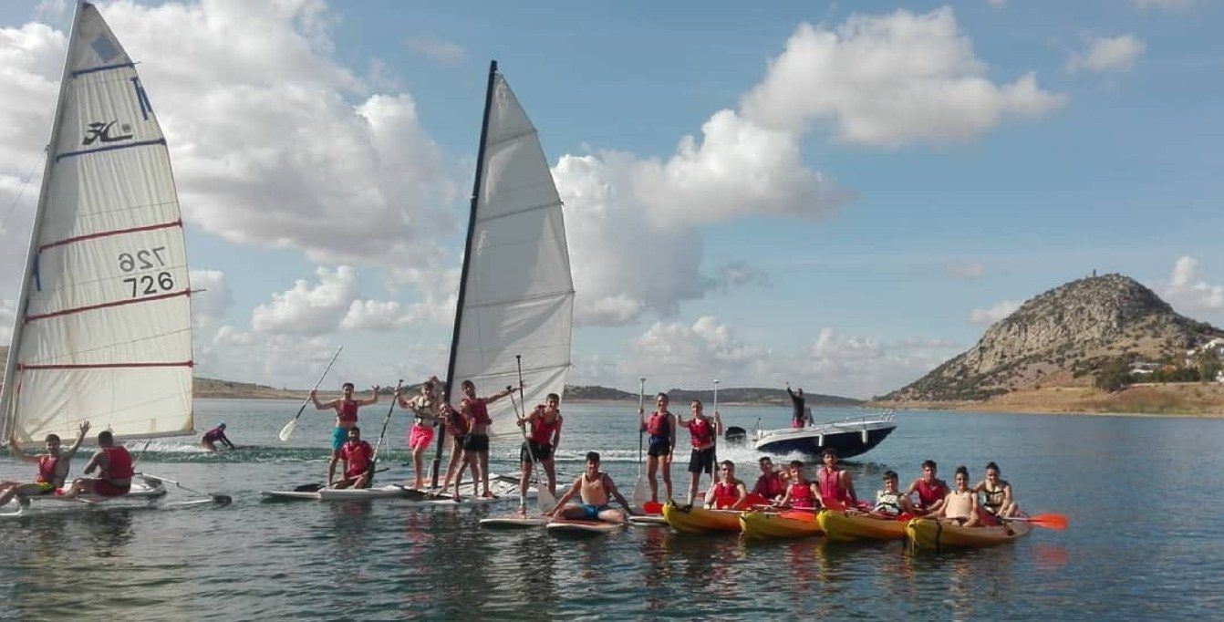 Grupo con veleros ligeros y piraguas en la orilla del embalse, con el cerro al fondo